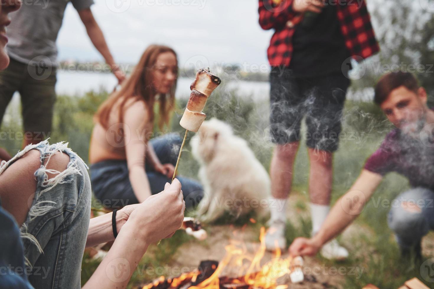 guimauve rôtie dans la mise au point de l'appareil photo. groupe de personnes pique-nique sur la plage. les amis s'amusent le week-end photo