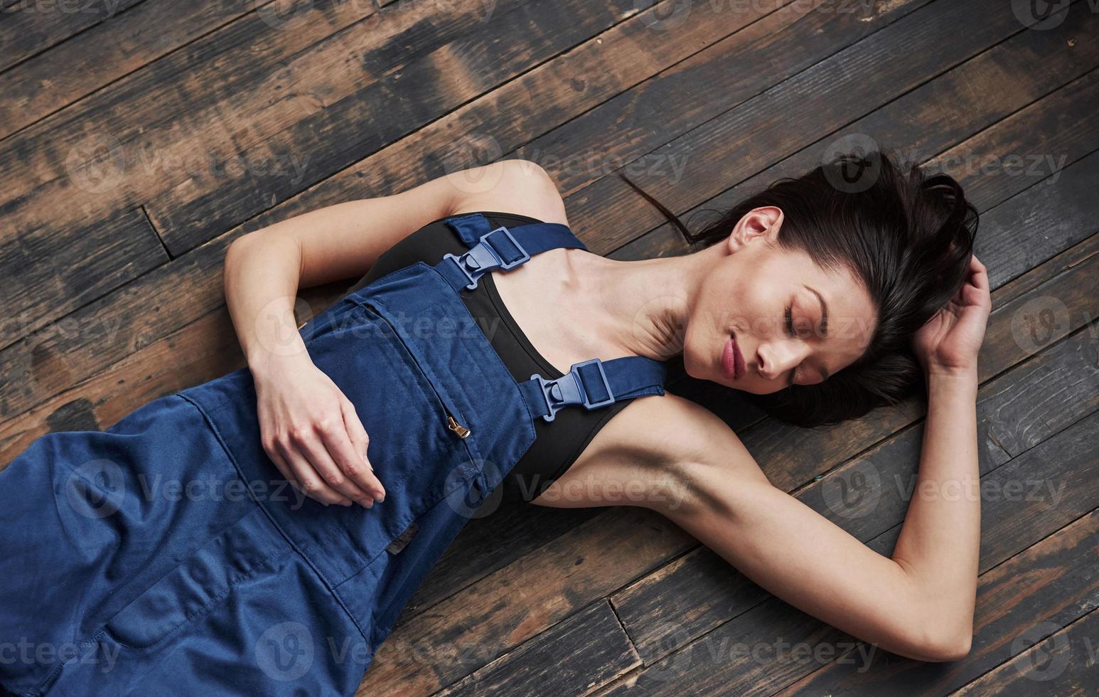 les yeux fermés. fille en uniforme bleu pour le travail est allongée sur un plancher en bois se détendre photo
