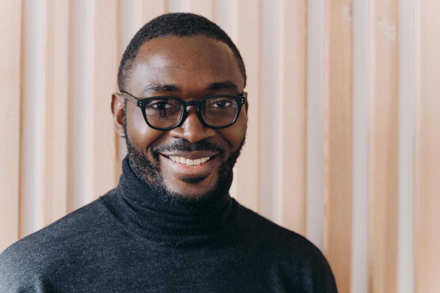 élégant homme d'affaires afro-américain confiant dans des verres posant debout dans un bureau moderne photo