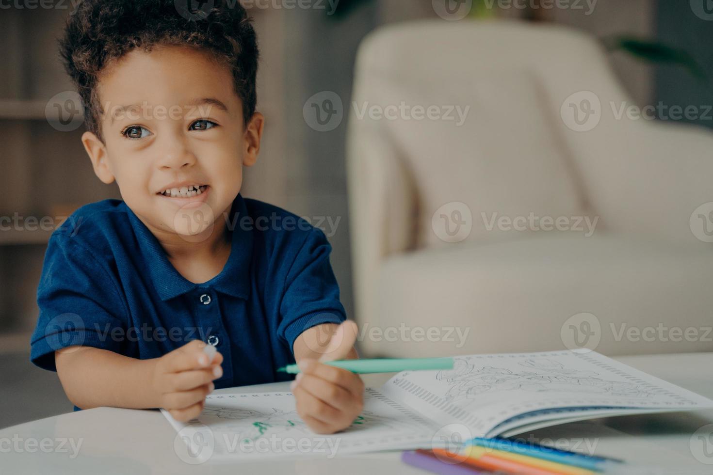 mignon petit garçon afro-américain en t-shirt polo bleu foncé peinture livre de coloriage à la maison photo