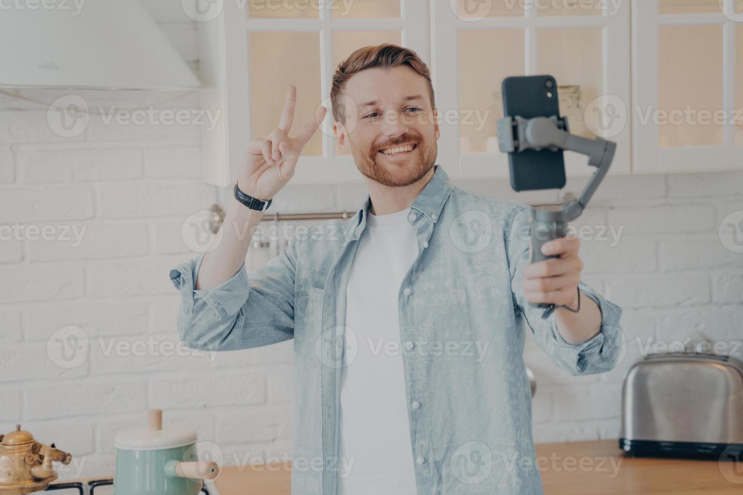 beau jeune homme brunete souriant avec chaume faisant selfie dans la cuisine photo