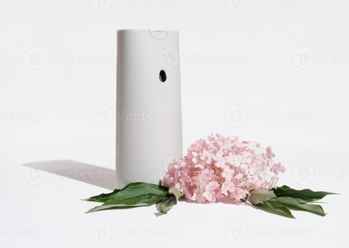 assainisseur d'air automatique à côté de fleurs d'hortensia rose sur fond blanc. parfums d'ambiance et parfums d'ambiance pour une ambiance cosy photo