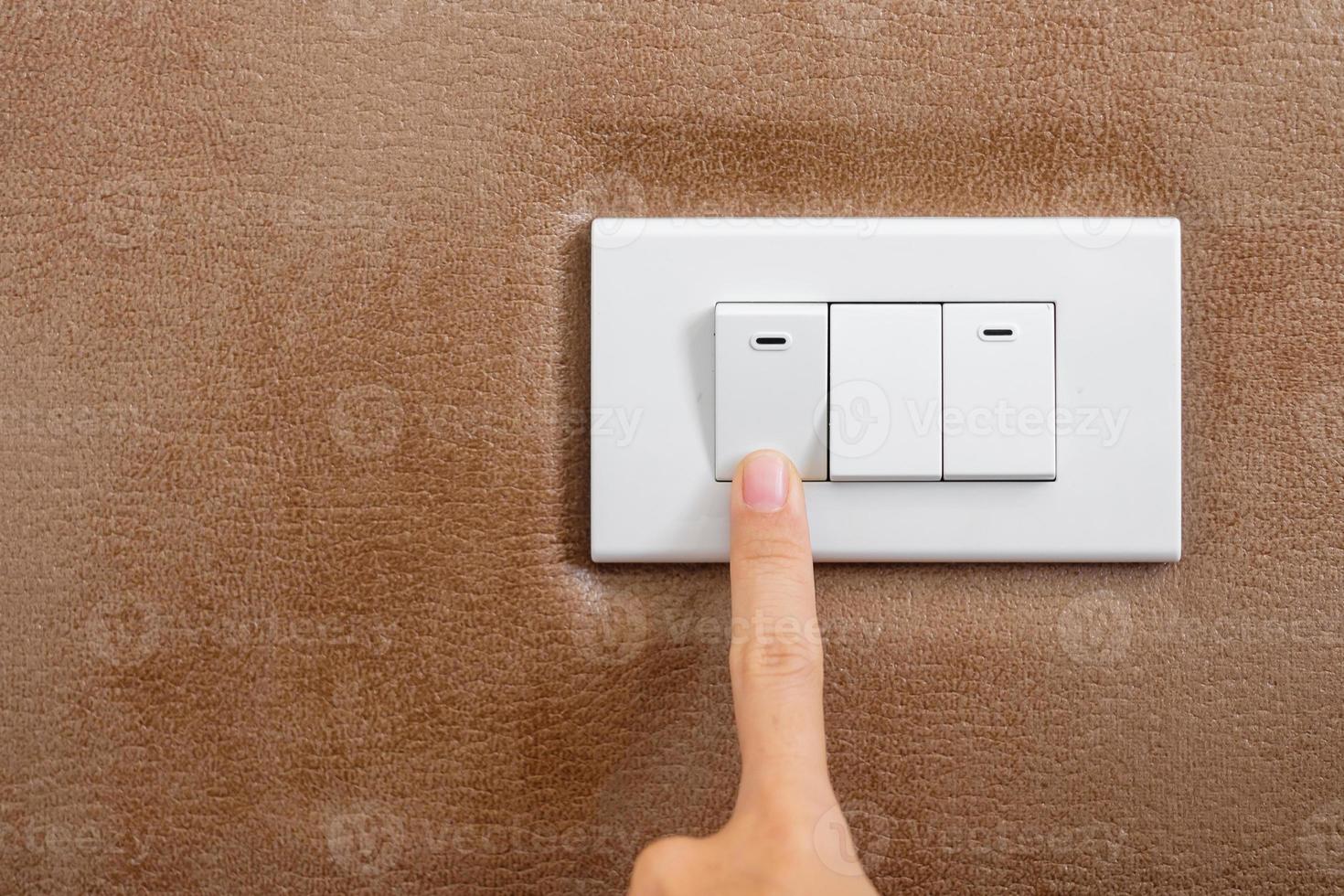 le doigt allume ou éteint l'interrupteur d'éclairage sur le mur à la maison. concepts d'économie d'énergie, d'électricité, d'électricité et de style de vie photo