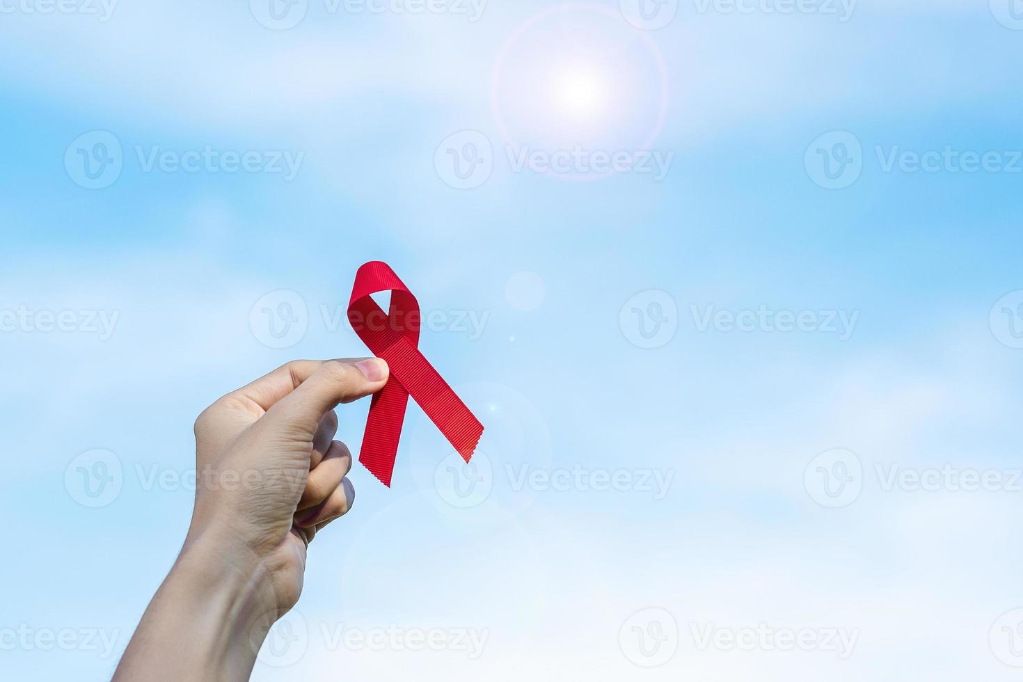 main tenant un ruban rouge pour soutenir les personnes vivant et malades. concept de soins de santé et de rapports sexuels protégés. décembre journée mondiale du sida et mois de sensibilisation au cancer du myélome multiple photo