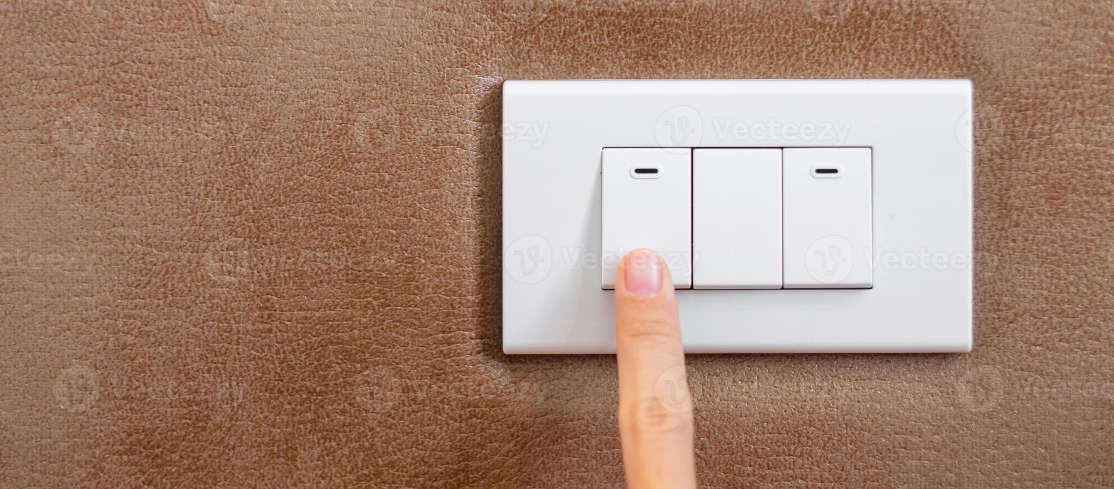 le doigt allume ou éteint l'interrupteur d'éclairage sur le mur à la maison. concepts d'économie d'énergie, d'électricité, d'électricité et de style de vie photo