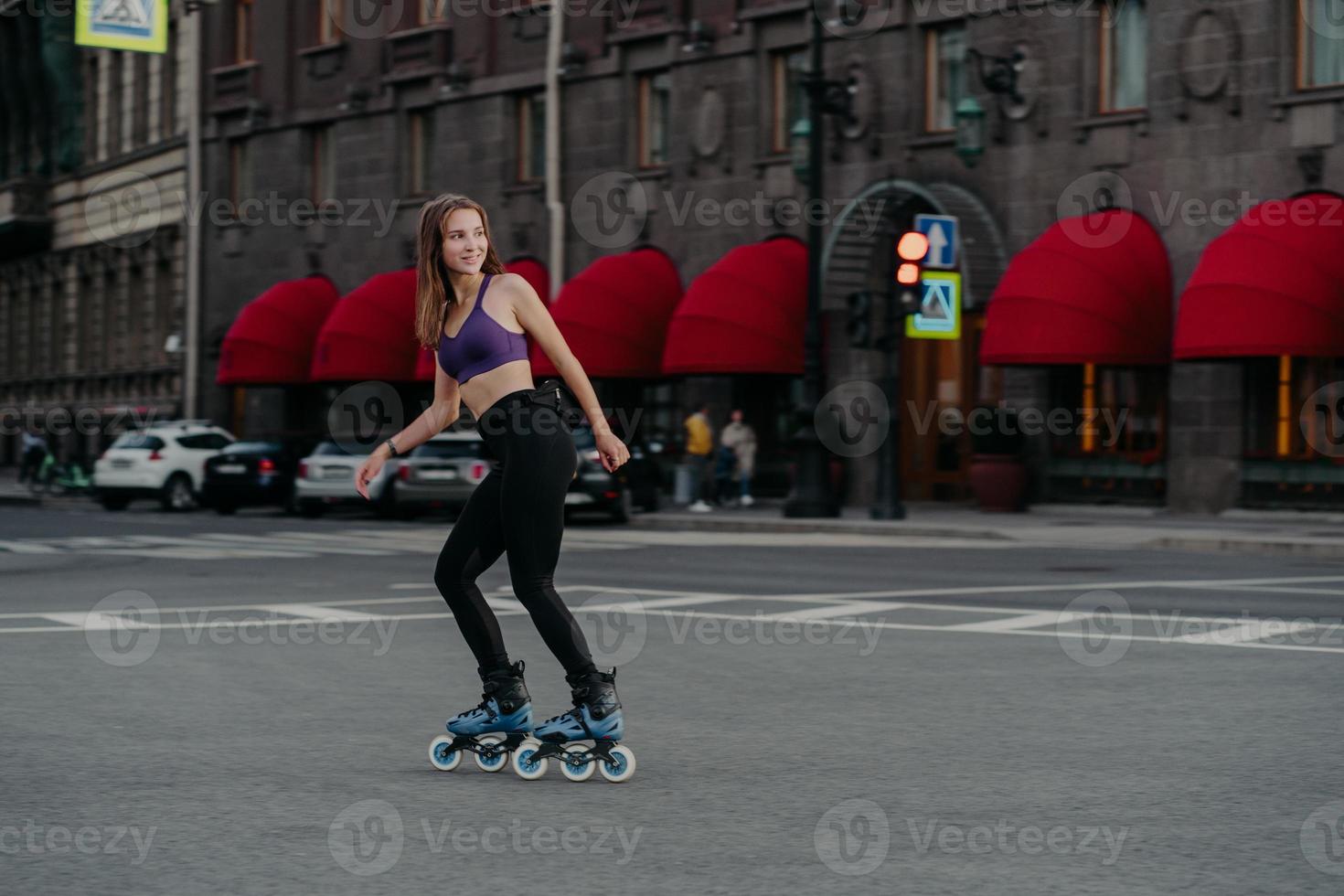 une femme sportive heureuse monte sur des rouleaux en milieu urbain mène un mode de vie sain vêtu de vêtements de sport regarde ailleurs a une expression joyeuse aime l'entraînement physique. activité sportive passe-temps loisirs photo