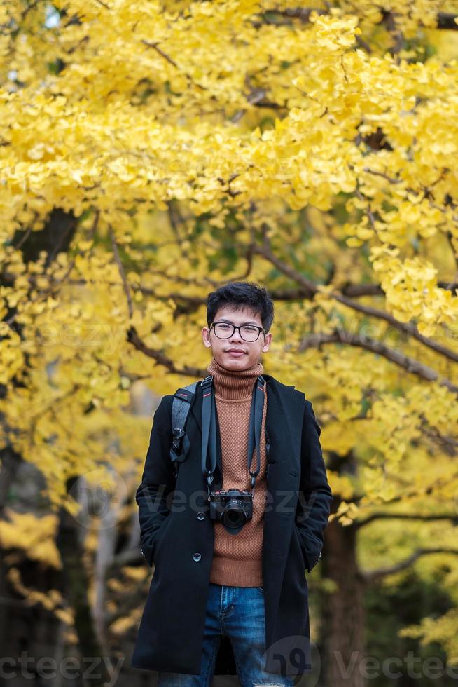 homme heureux profiter au parc en plein air en automne, voyageur asiatique en manteau et appareil photo sur fond de feuilles de ginkgo jaune