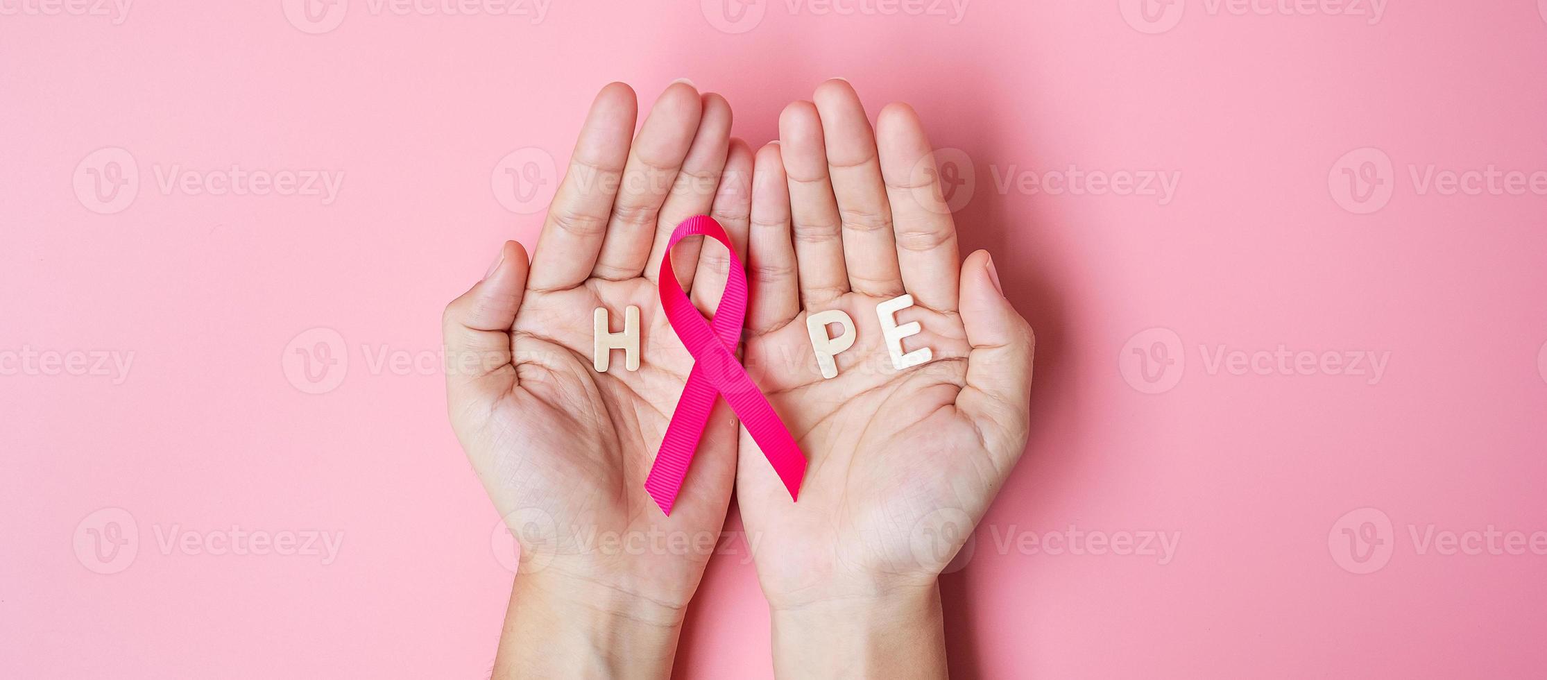 octobre mois de sensibilisation au cancer du sein, main de femme adulte tenant un ruban rose sur fond rose pour soutenir les personnes vivant et malades. concept de la journée internationale des femmes, des mères et du cancer photo