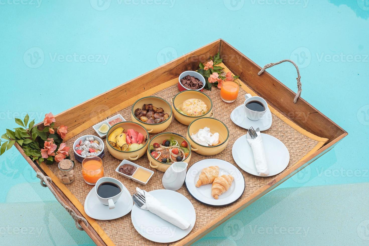 plateau de petit-déjeuner flottant dans la piscine d'un hôtel de luxe ou d'une villa tropicale, fruits, croissant, café et jus d'orange. été exotique, détente, voyage tropical et concept de vacances photo