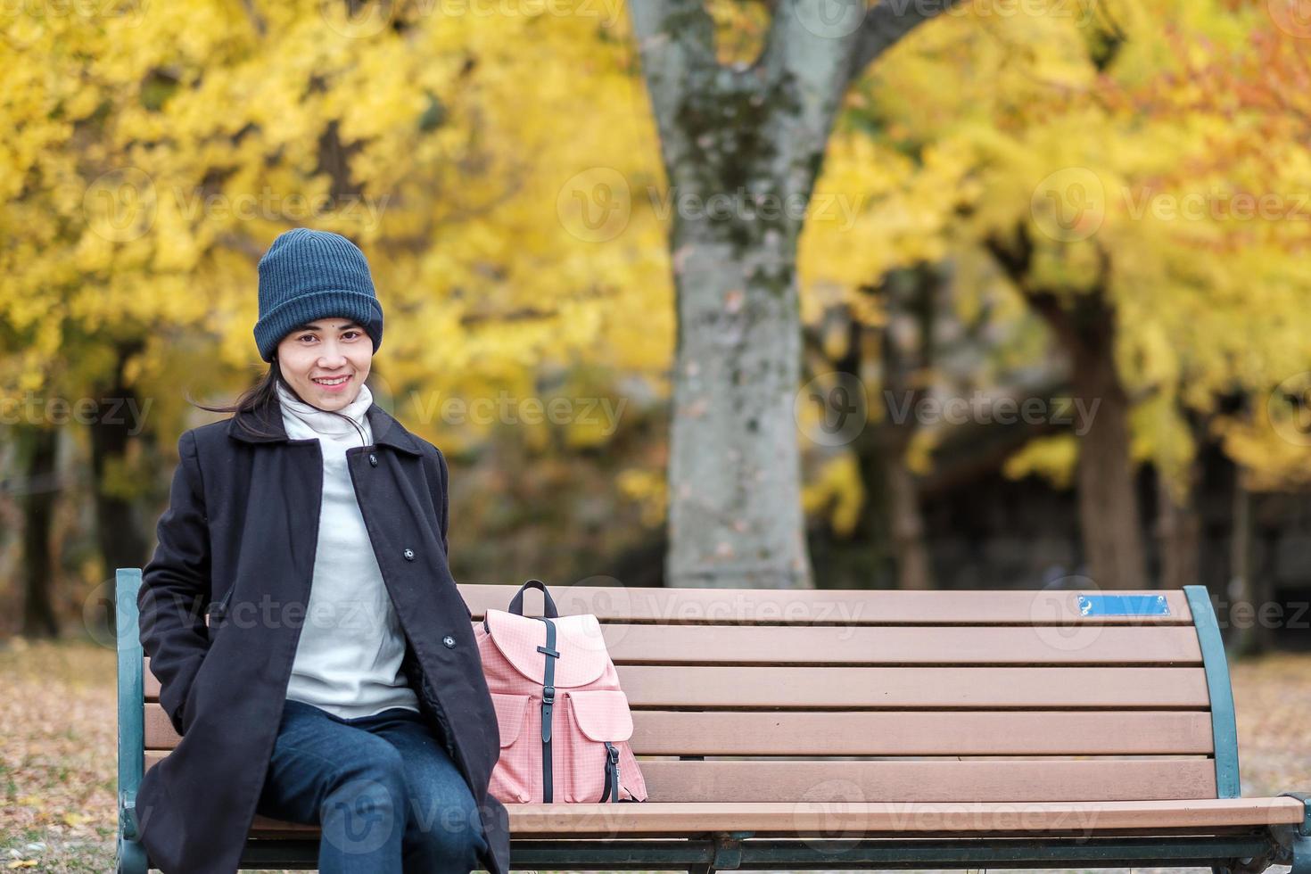 femme heureuse profiter du parc en plein air en automne, voyageur asiatique en manteau et chapeau sur fond de feuilles de ginkgo jaune photo