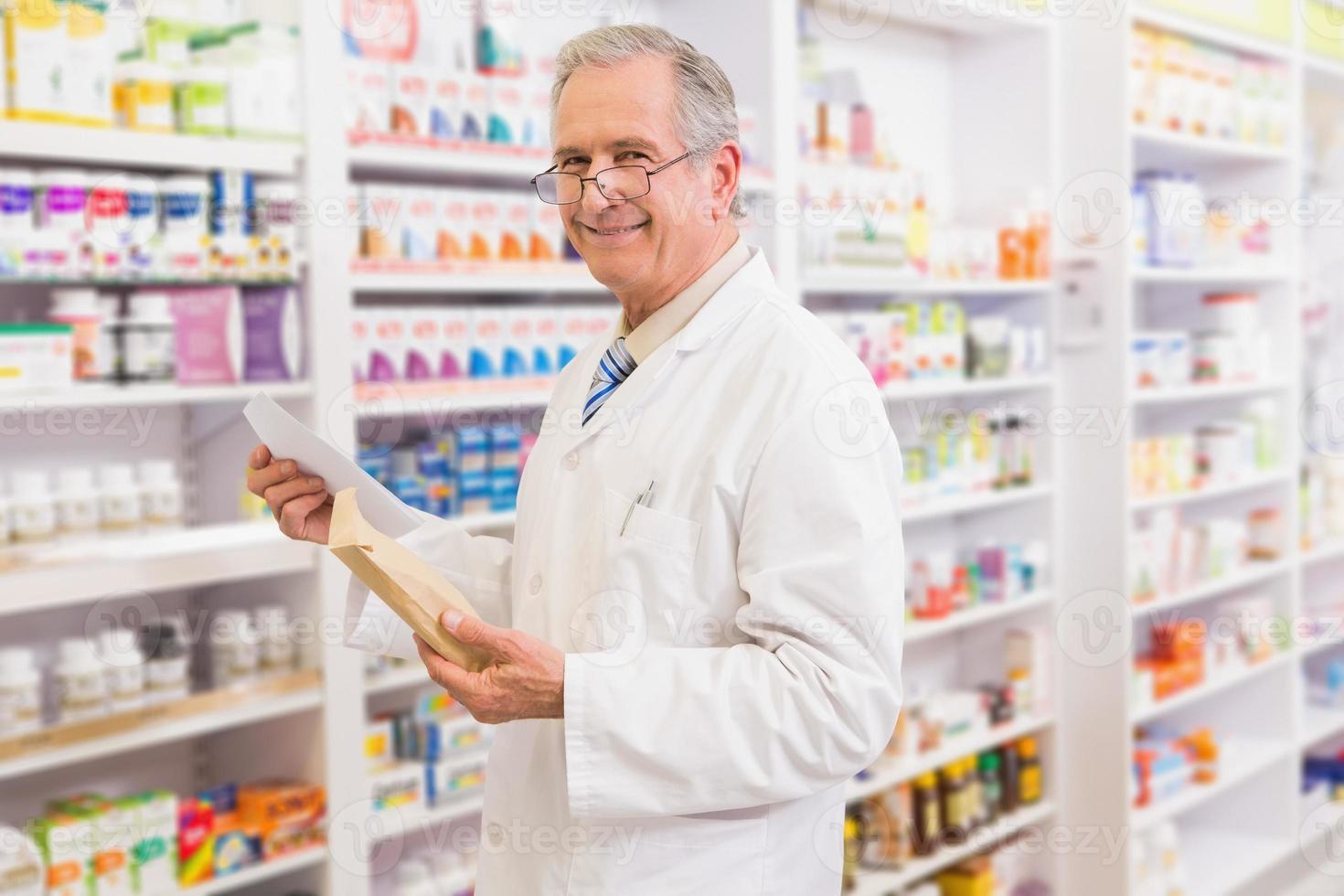 pharmacien senior souriant tenant enveloppe et prescription photo