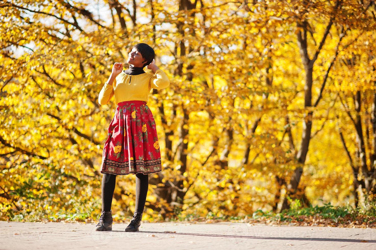 fille afro-américaine en robe jaune et rouge au parc d'automne doré. photo