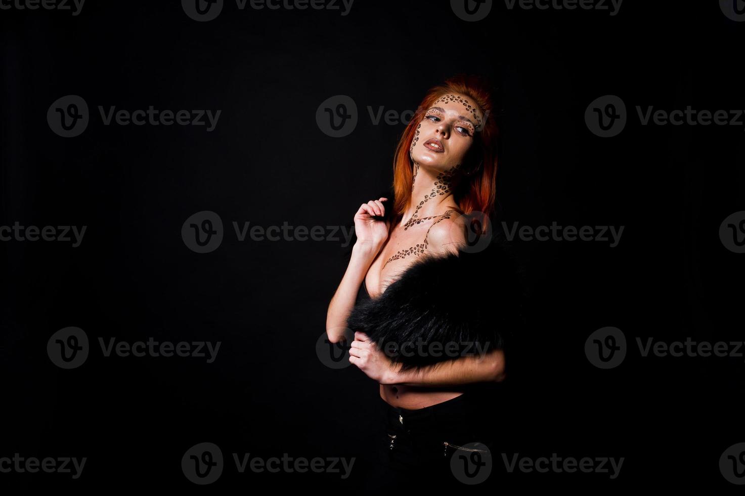 modèle de mode fille aux cheveux rouges avec à l'origine maquillage comme prédateur de léopard isolé sur noir. portrait d'atelier. photo
