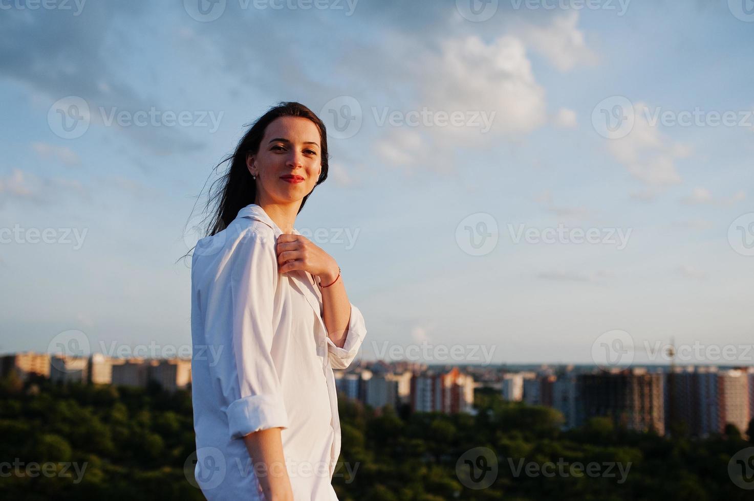 portrait d'une femme exceptionnelle en chemise blanche masculine posant au sommet du bâtiment avec un paysage charmant en arrière-plan. photo