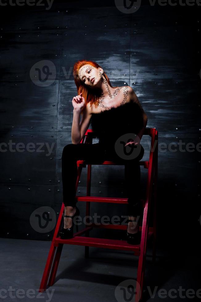 modèle de mode fille aux cheveux rouges avec à l'origine maquillage comme prédateur de léopard contre le mur d'acier. portrait en studio sur échelle. photo