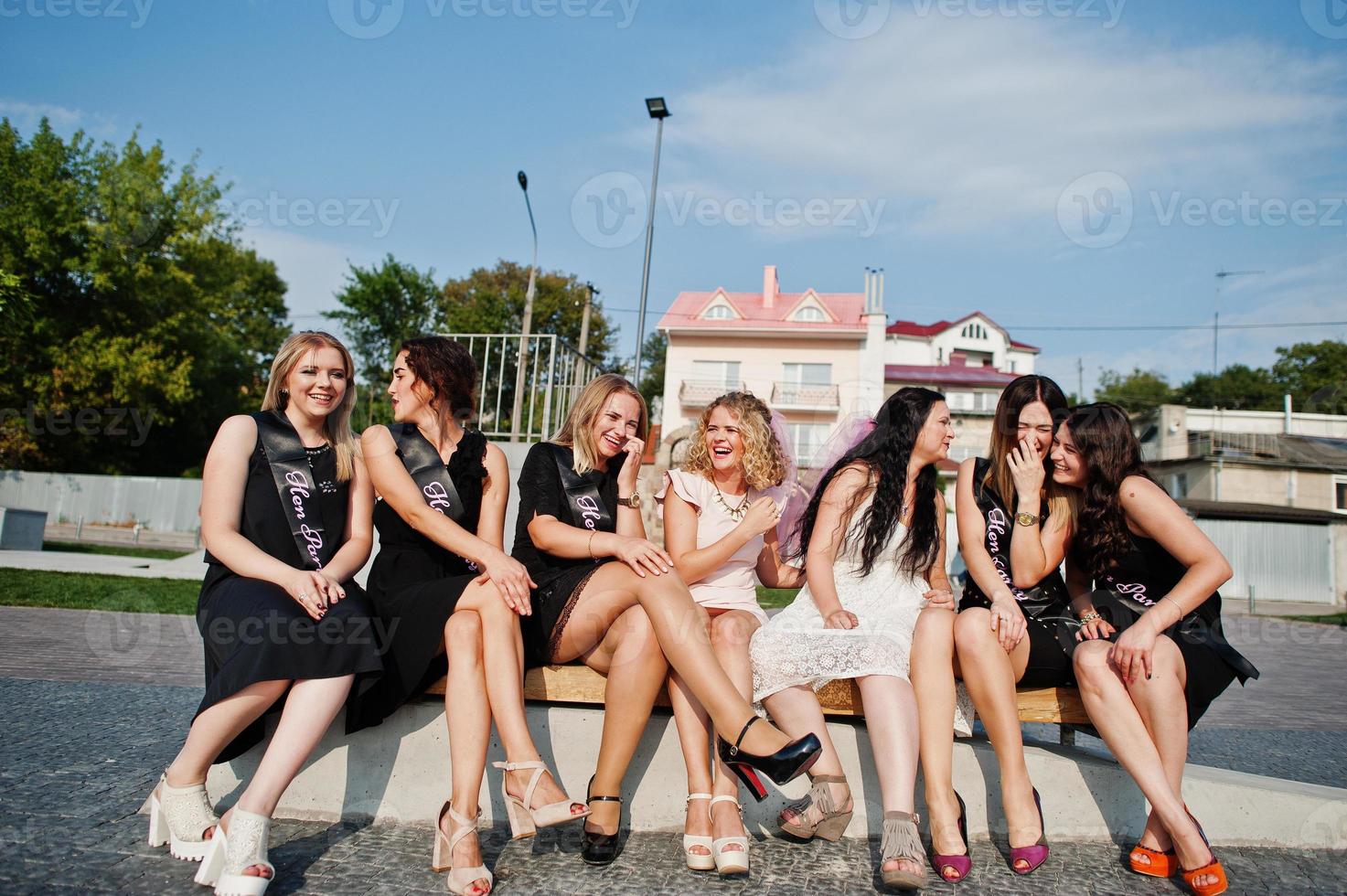 groupe de 7 filles portant du noir et 2 mariées assises sur un banc et s'amusant à la fête de poule. photo