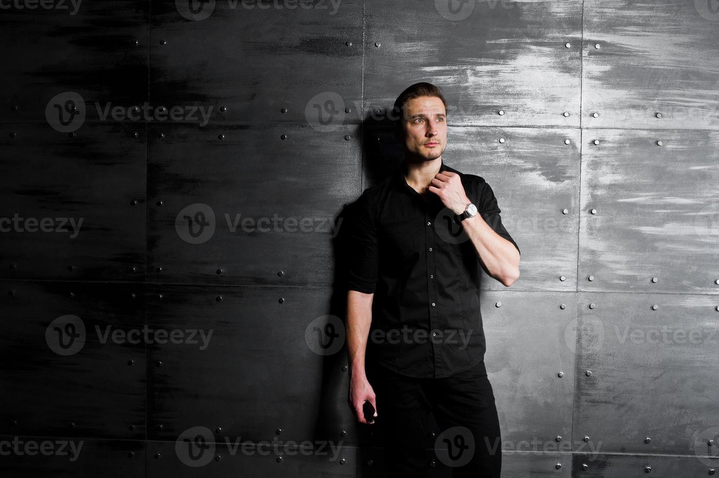 portrait en studio d'un homme élégant portant une chemise noire contre un mur en acier. photo