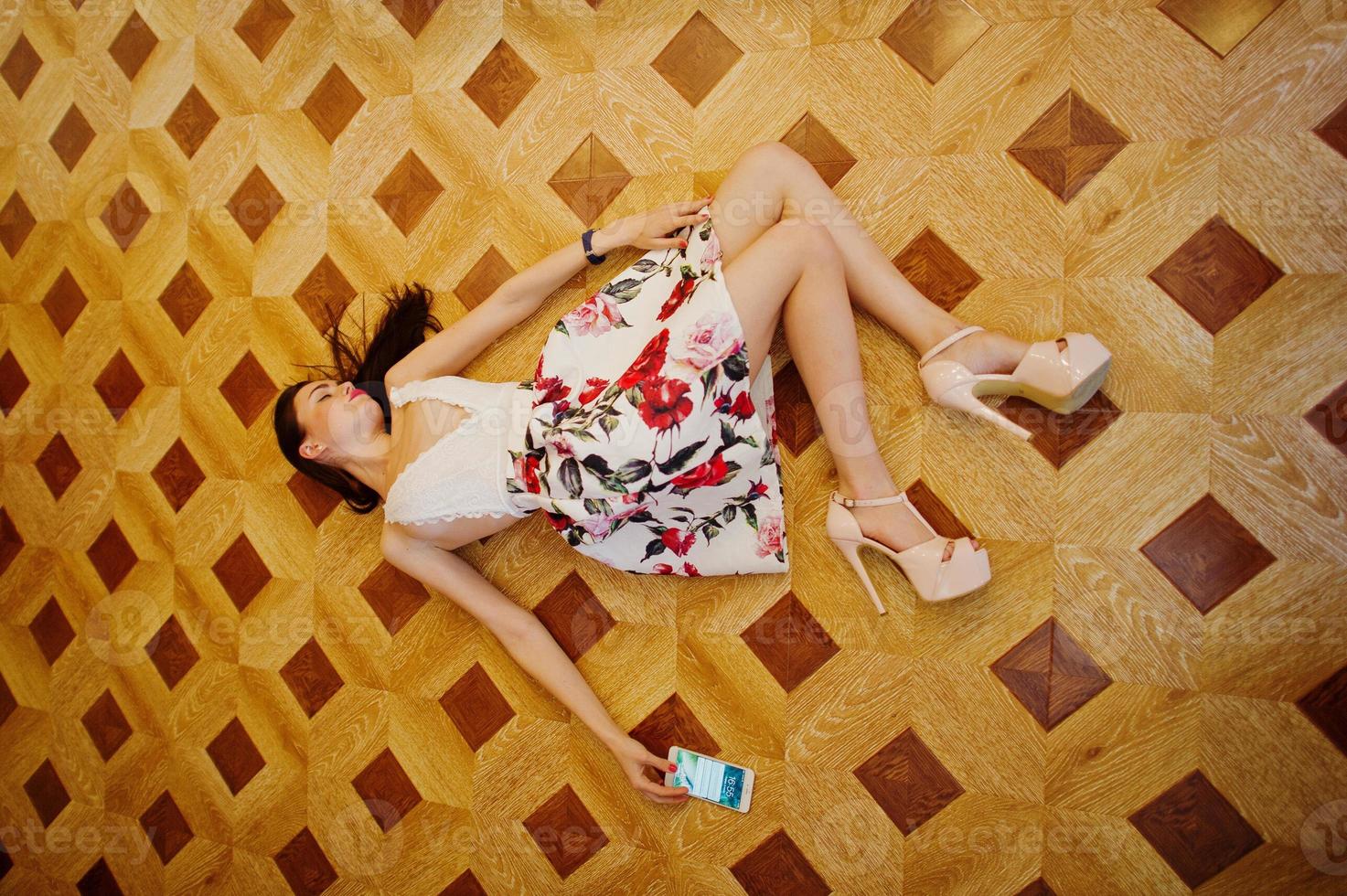 portrait d'une superbe jeune femme en robe magnifique allongée sur le sol avec son smartphone. photo