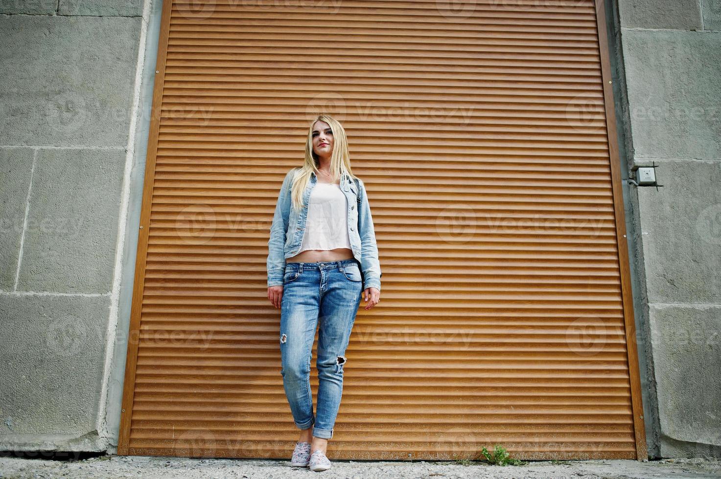 fille blonde porter sur une veste en jean avec sac à dos posé contre l'obturateur orange. photo