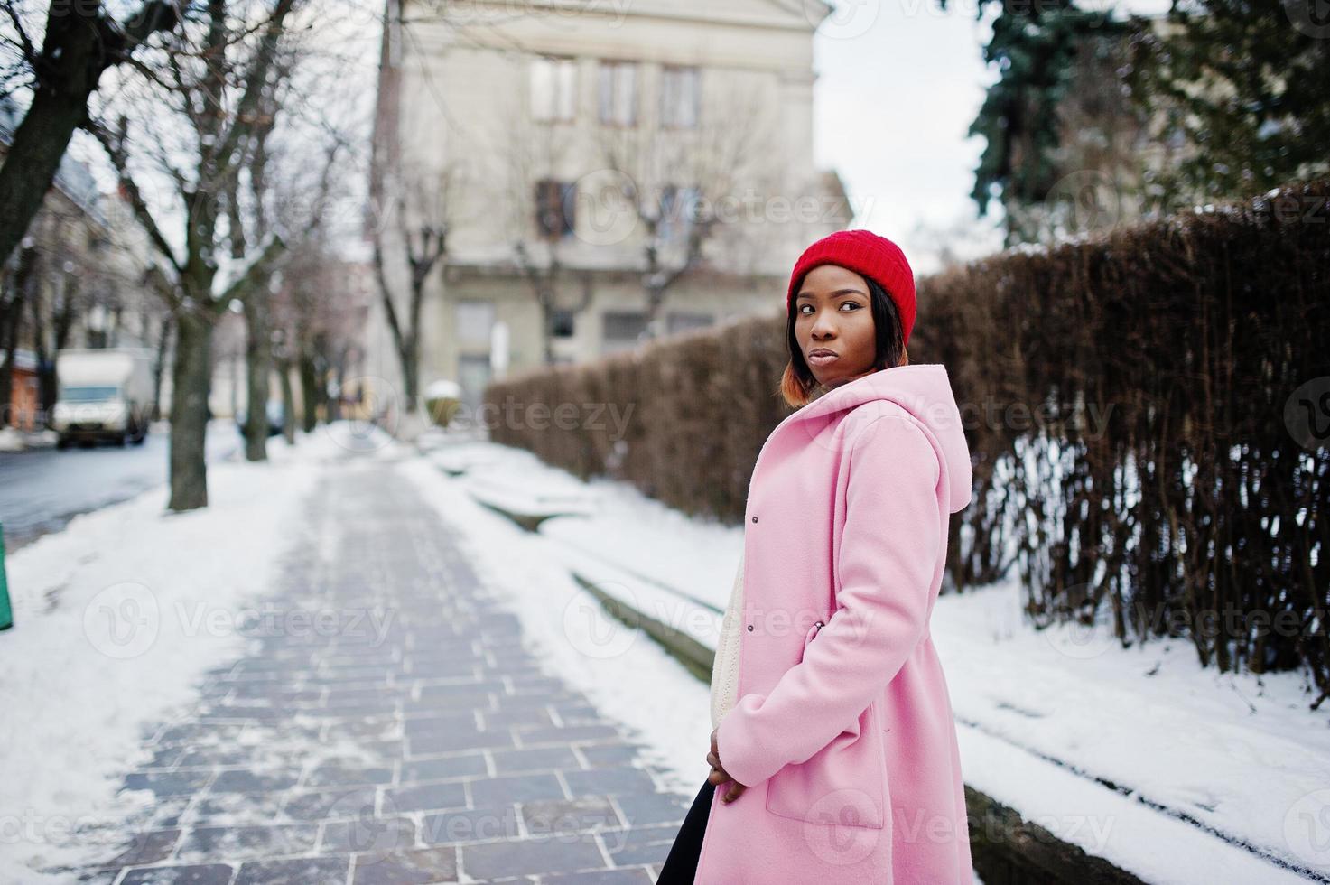 fille afro-américaine au chapeau rouge et manteau rose dans la rue de la ville le jour de l'hiver. photo