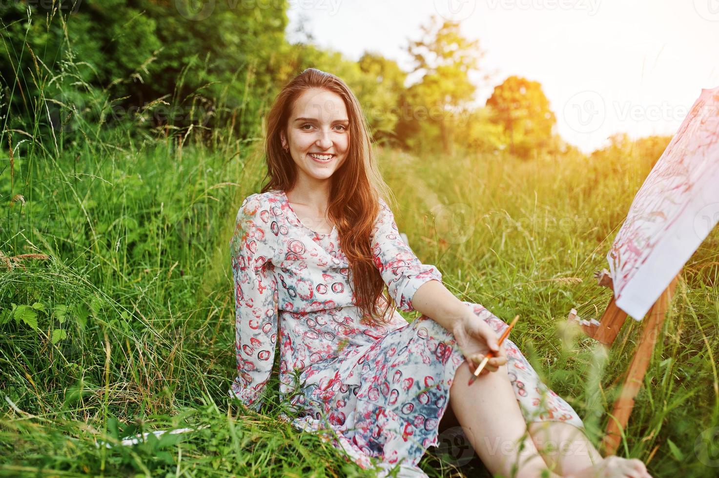 portrait d'une magnifique jeune femme heureuse en belle robe assise sur l'herbe et peinture sur papier à l'aquarelle. photo