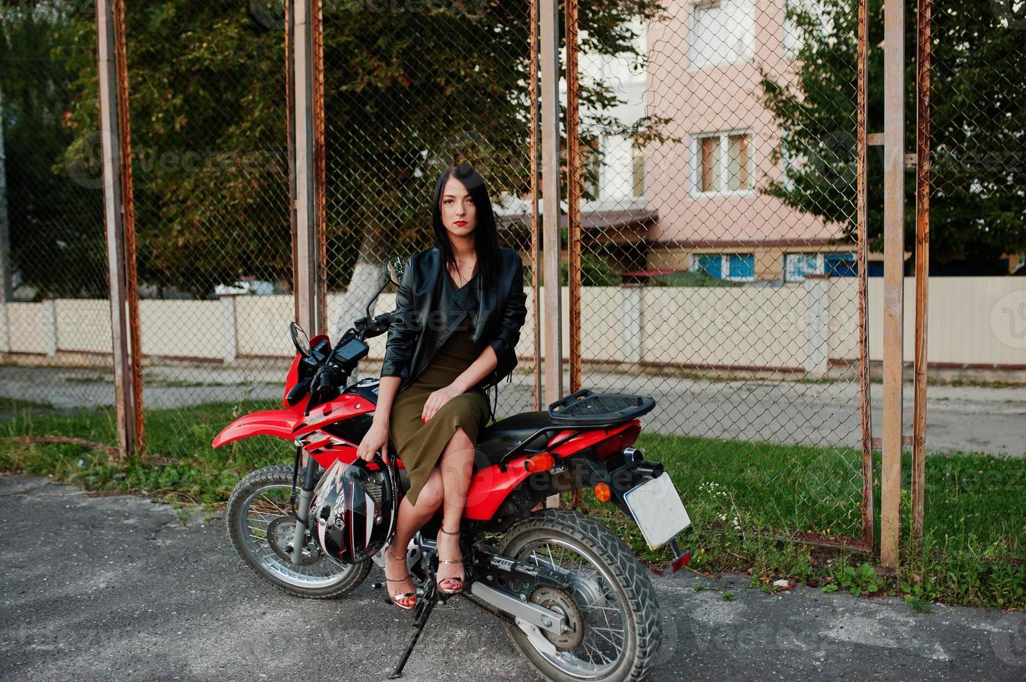 portrait d'une femme cool et géniale en robe et veste en cuir noir assise sur une moto rouge cool. photo