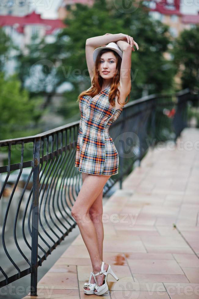 étonnantes longues jambes avec des talons hauts fille portant un chapeau posant près des balustrades du bâtiment moderne. photo