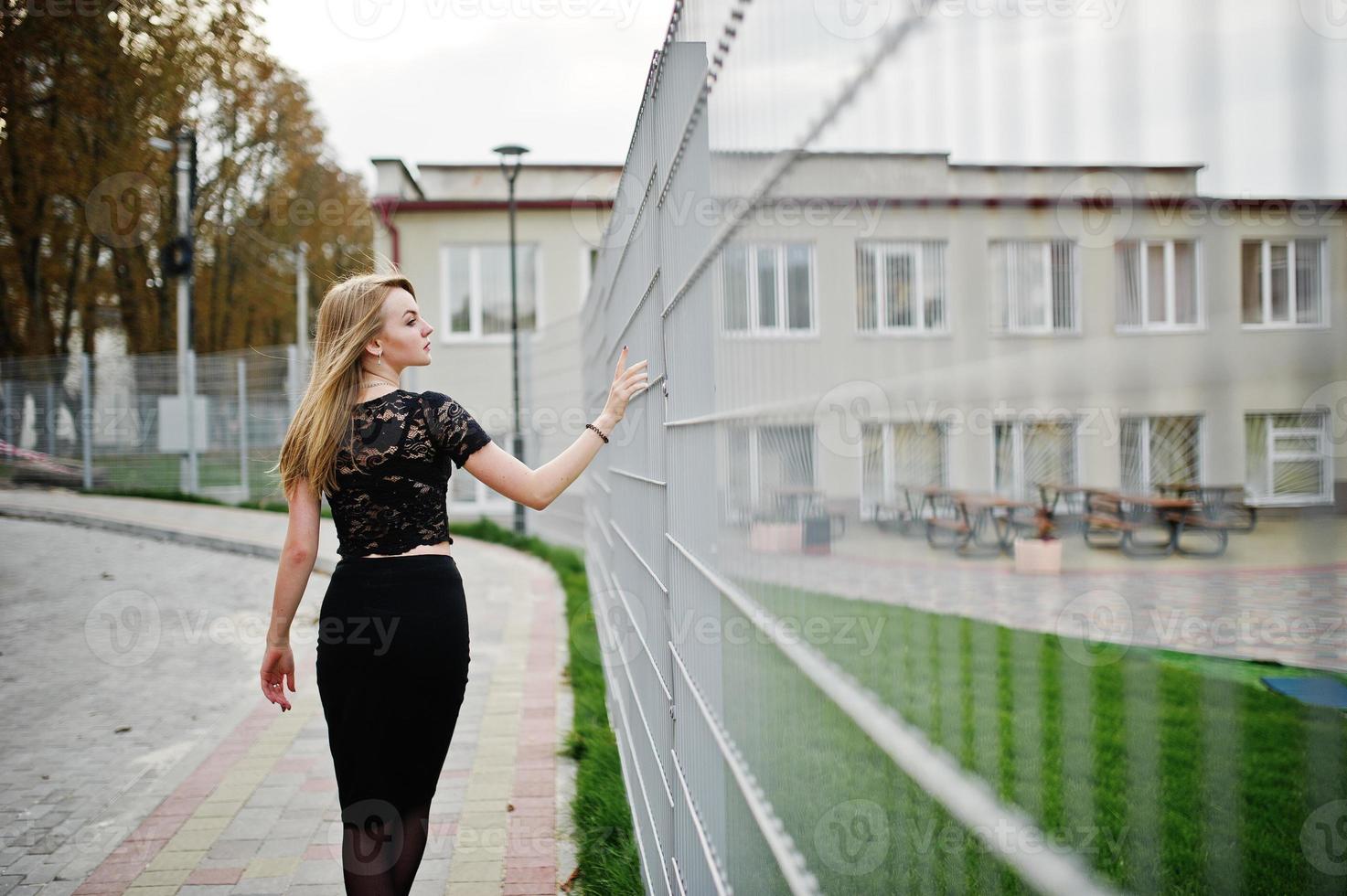 fille blonde élégante porter sur noir posant dans les rues de la ville contre la cage de fer. photo