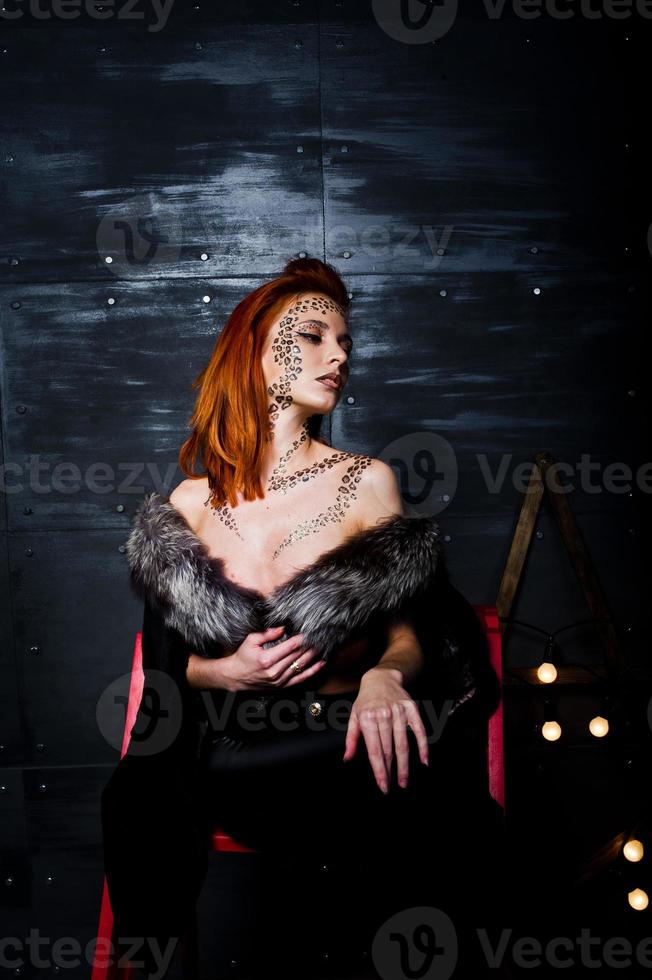 modèle de mode fille aux cheveux rouges avec à l'origine maquillage comme prédateur de léopard contre le mur d'acier. portrait en studio sur échelle. photo