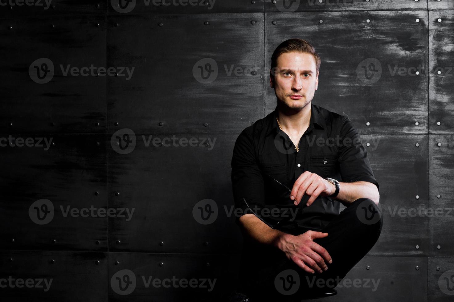 portrait en studio d'un homme élégant portant une chemise noire contre un mur en acier. photo