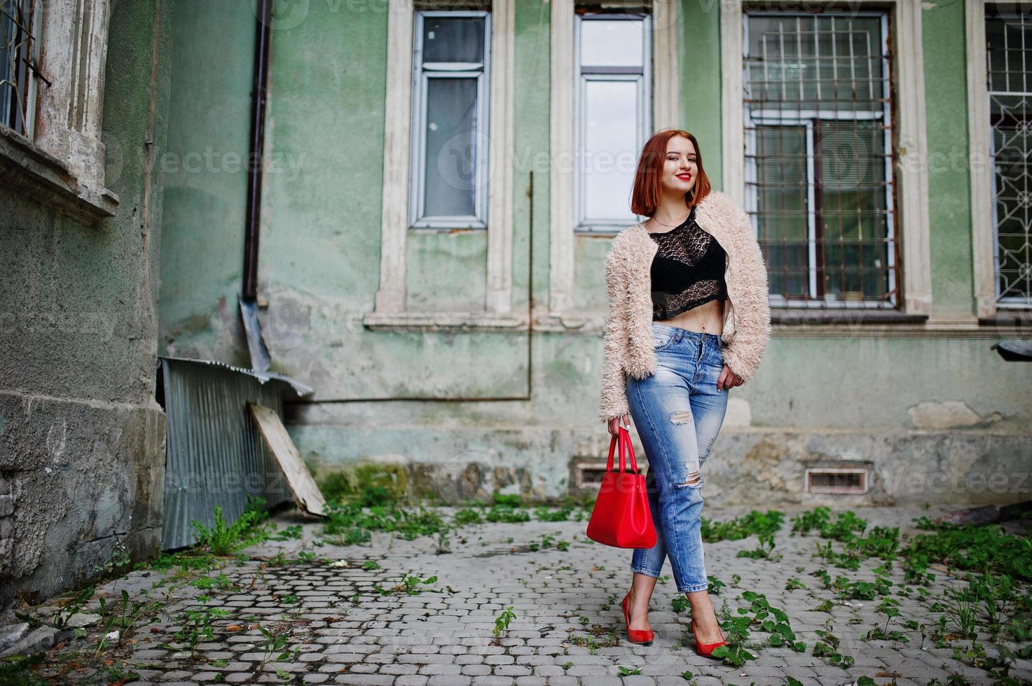 fille aux cheveux rouges avec sac à main rouge posé dans la rue de la ville. photo