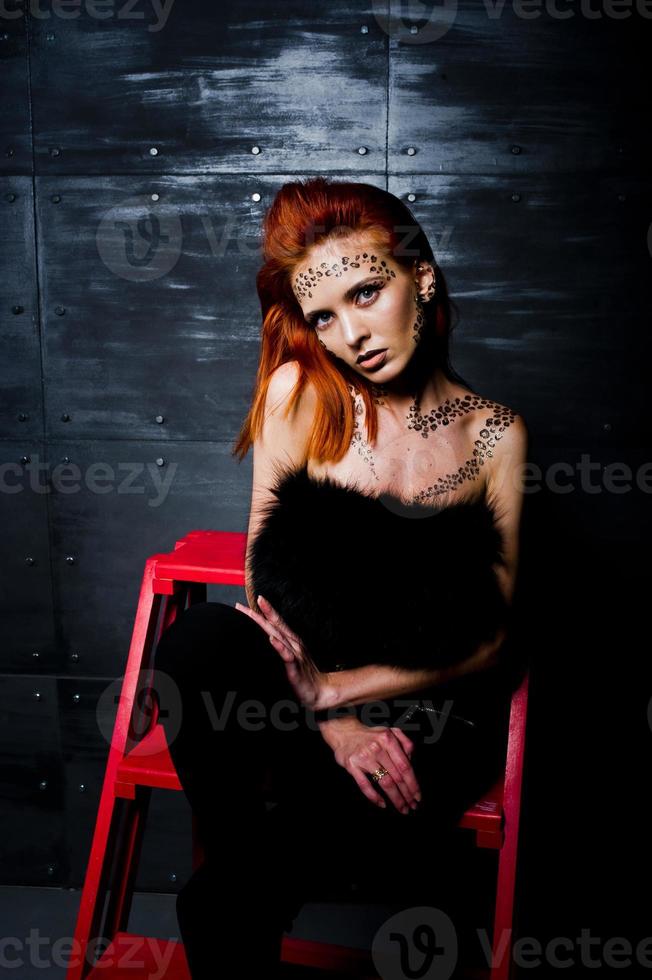 modèle de mode fille aux cheveux rouges avec à l'origine maquillage comme prédateur de léopard contre le mur d'acier. portrait en studio sur échelle. photo