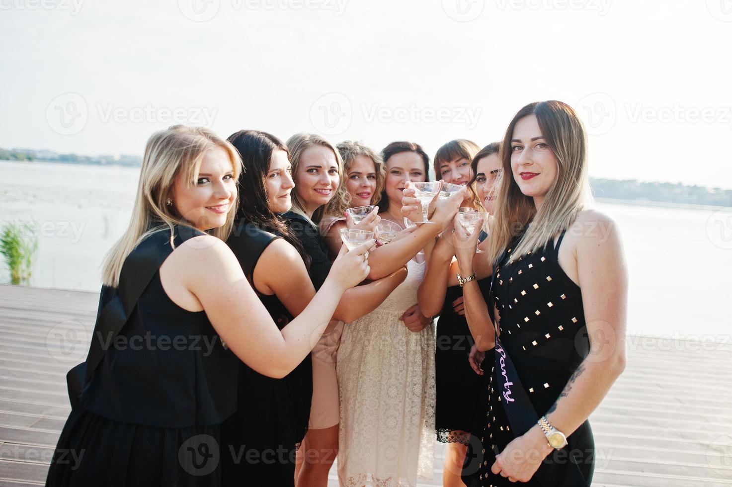 groupe de 8 filles portent du noir et 2 mariées à la fête de poule contre la plage ensoleillée buvant du champagne. photo