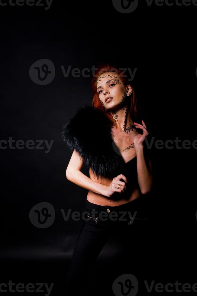 modèle de mode fille aux cheveux rouges avec à l'origine maquillage comme prédateur de léopard isolé sur noir. portrait d'atelier. photo