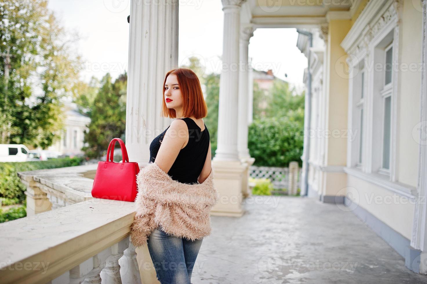 fille aux cheveux rouges avec sac à main rouge posé près de la maison vintage. photo