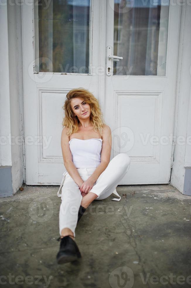 fille modèle blonde bouclée élégante porter sur blanc posant contre la vieille porte en bois. photo