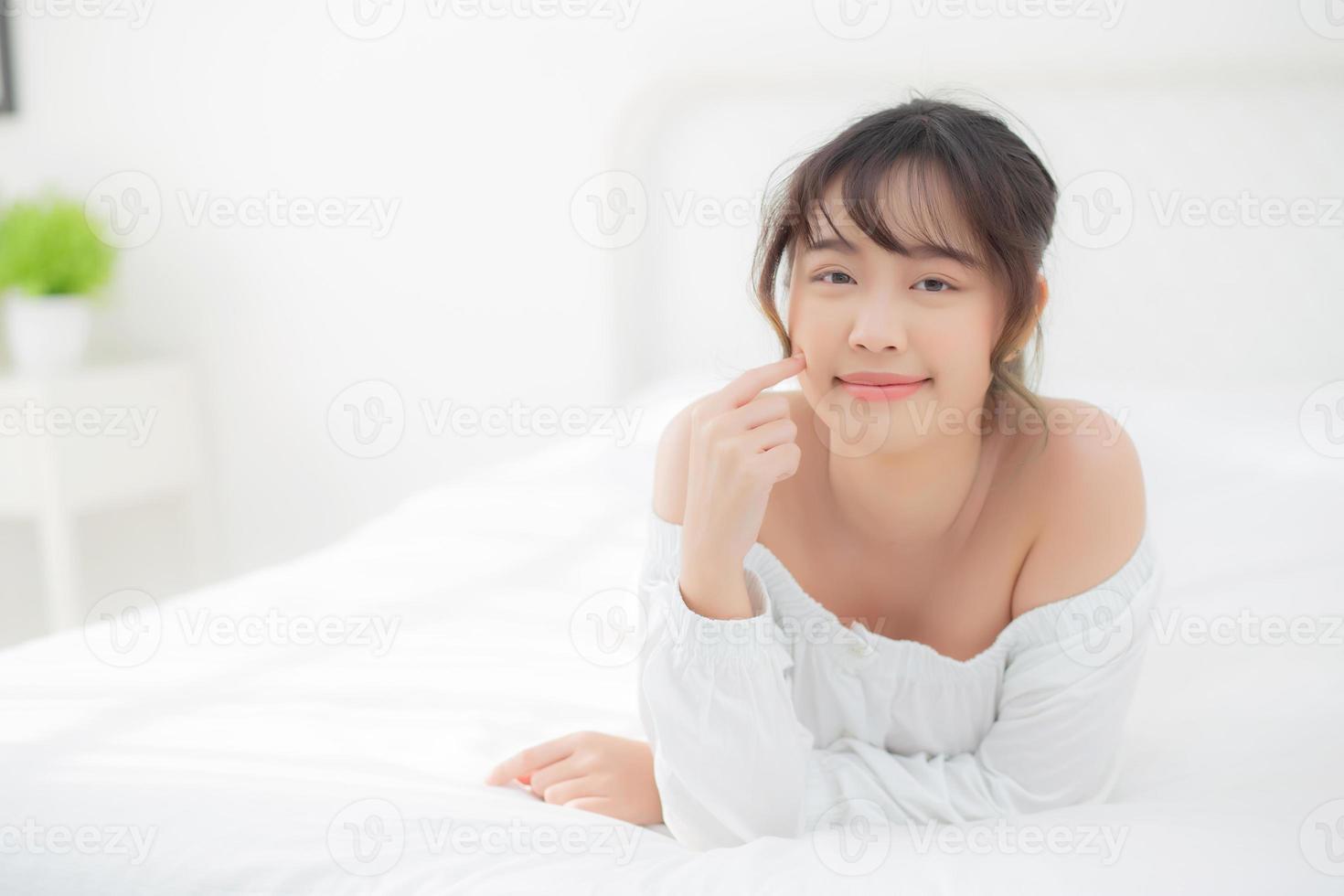 portrait belle jeune femme asiatique sourire tout en se réveillant en bonne santé et bien-être le matin dans la chambre à coucher, beauté asie fille allongée soins de la peau et maquillage cosmétique avec concept heureux, mode de vie et détente. photo