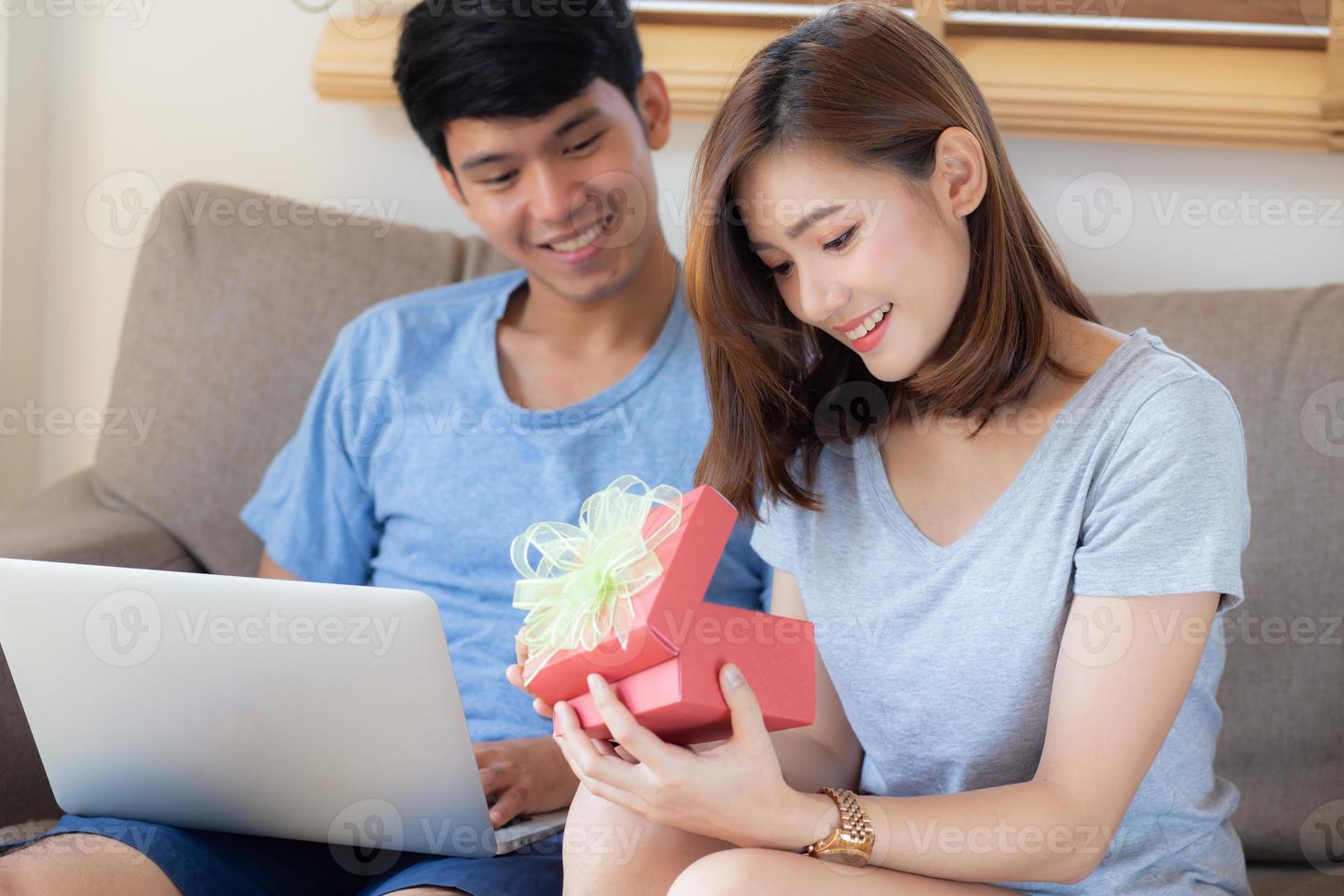 jeune couple asiatique fête son anniversaire ensemble, homme asiatique donnant une boîte-cadeau à une femme pour la surprendre dans le salon, femme se sentant heureuse et excitée anniversaire, concept de vacances saint valentin. photo