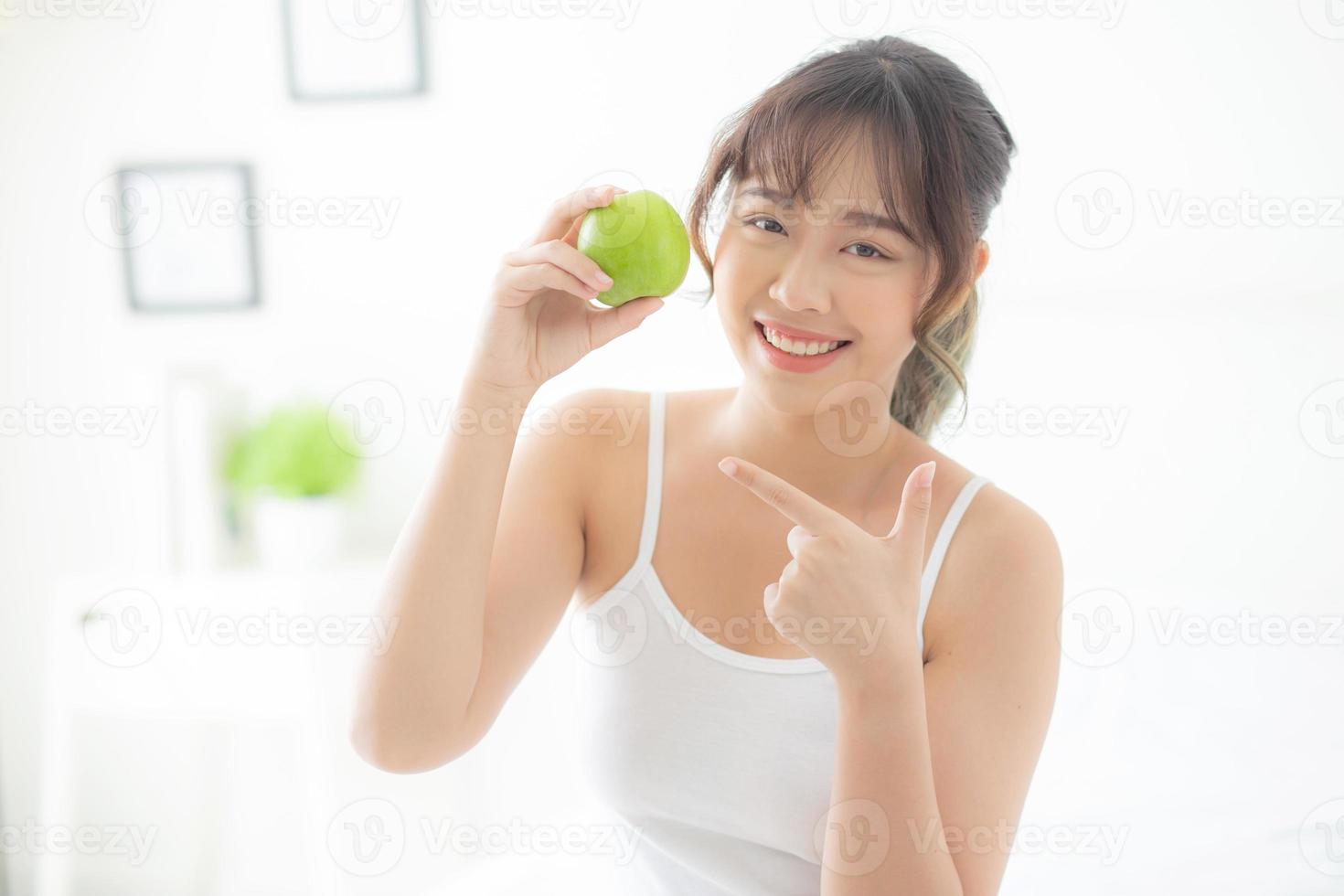 beau portrait jeune femme asiatique tenant et pointant des pommes vertes dans la chambre à la maison, mode de vie de nutrition fille saine et soins perte de poids, concept de santé et de bien-être. photo