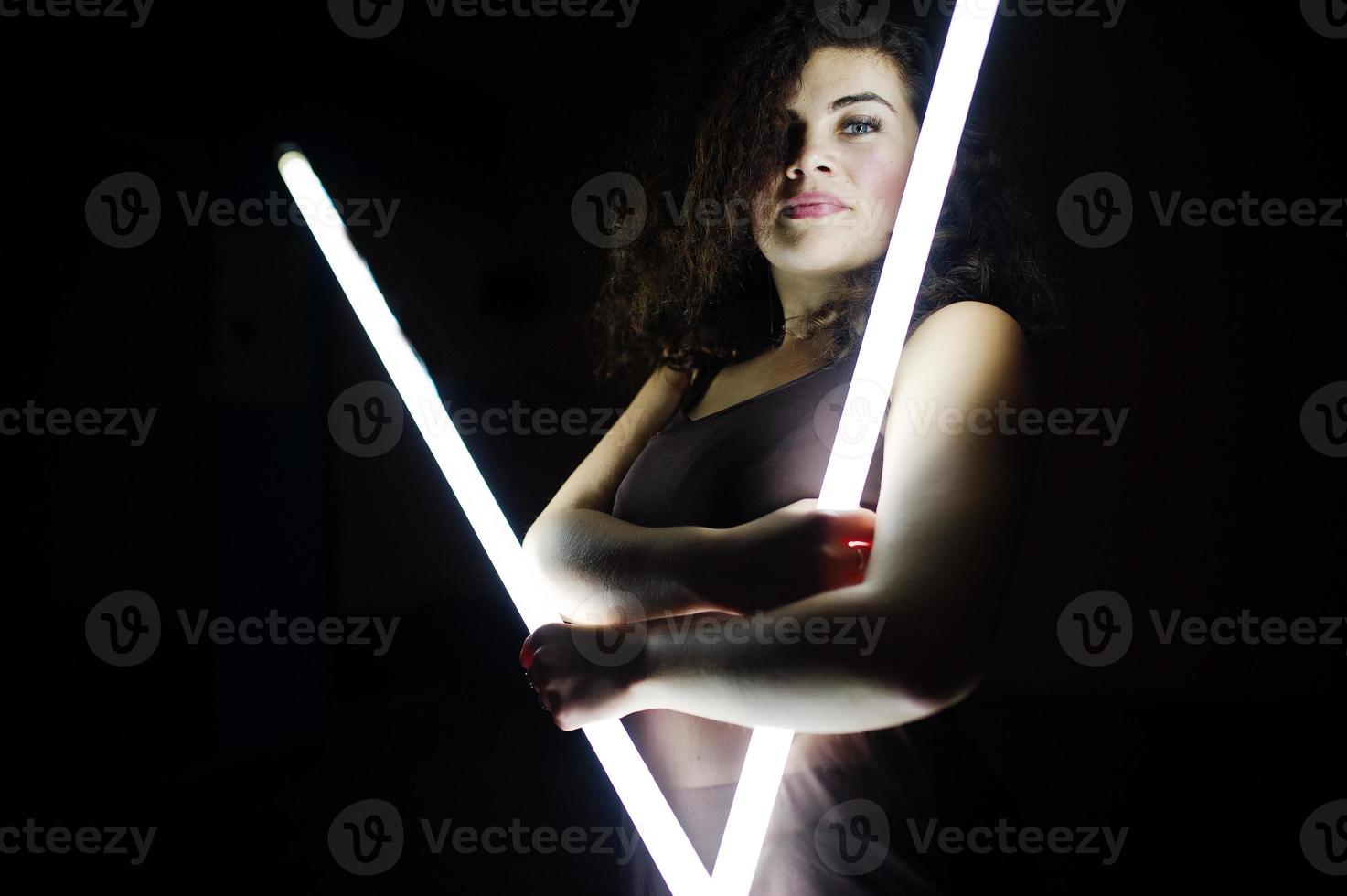 modèle de taille plus brune bouclée avec deux longues lampes à led dans la chambre noire. photo