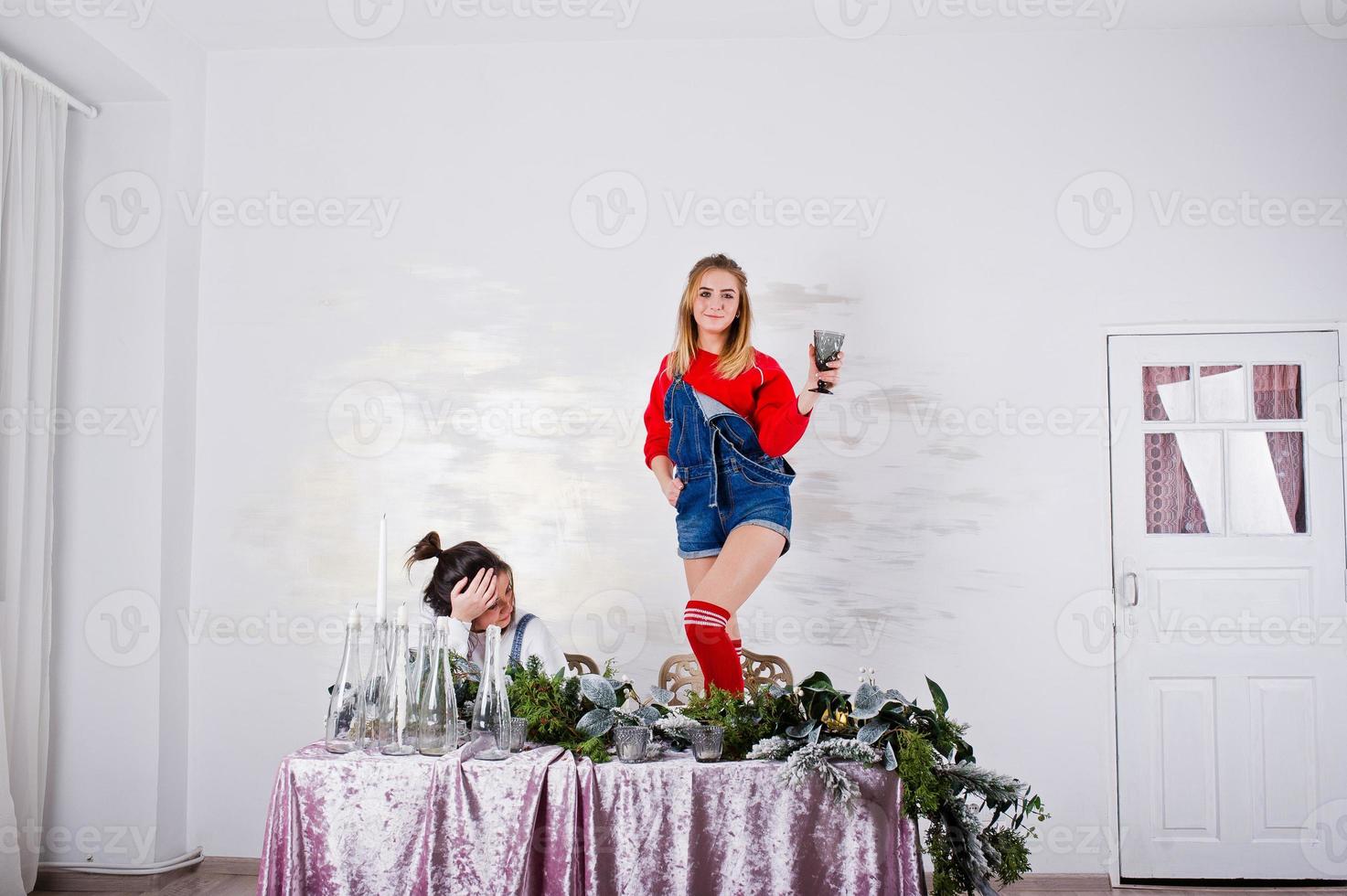 deux jolies amies amusantes portent des shorts en jean et des guêtres contre une table avec une décoration de nouvel an. photo