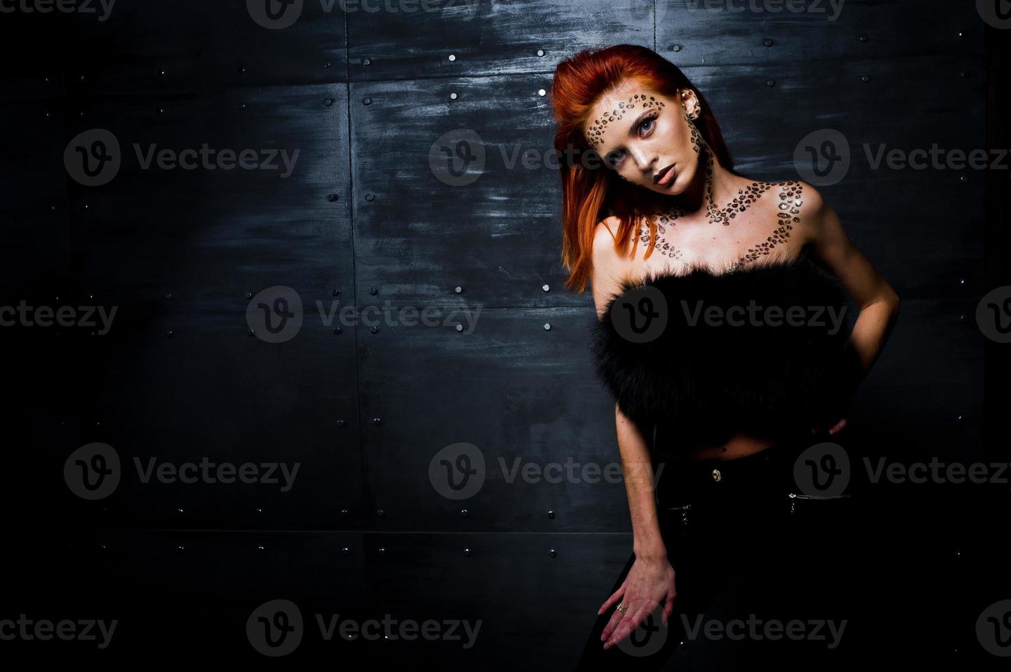 modèle de mode fille aux cheveux rouges avec à l'origine maquillage comme prédateur de léopard contre le mur d'acier. portrait d'atelier. photo