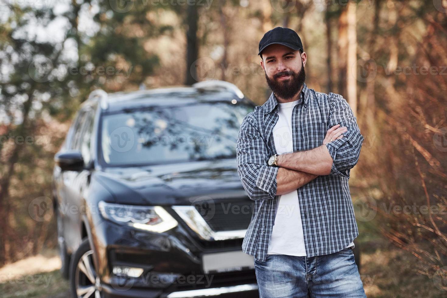 heureux propriétaire d'une automobile de luxe. homme barbu près de sa toute nouvelle voiture noire dans la forêt. notion de vacances photo