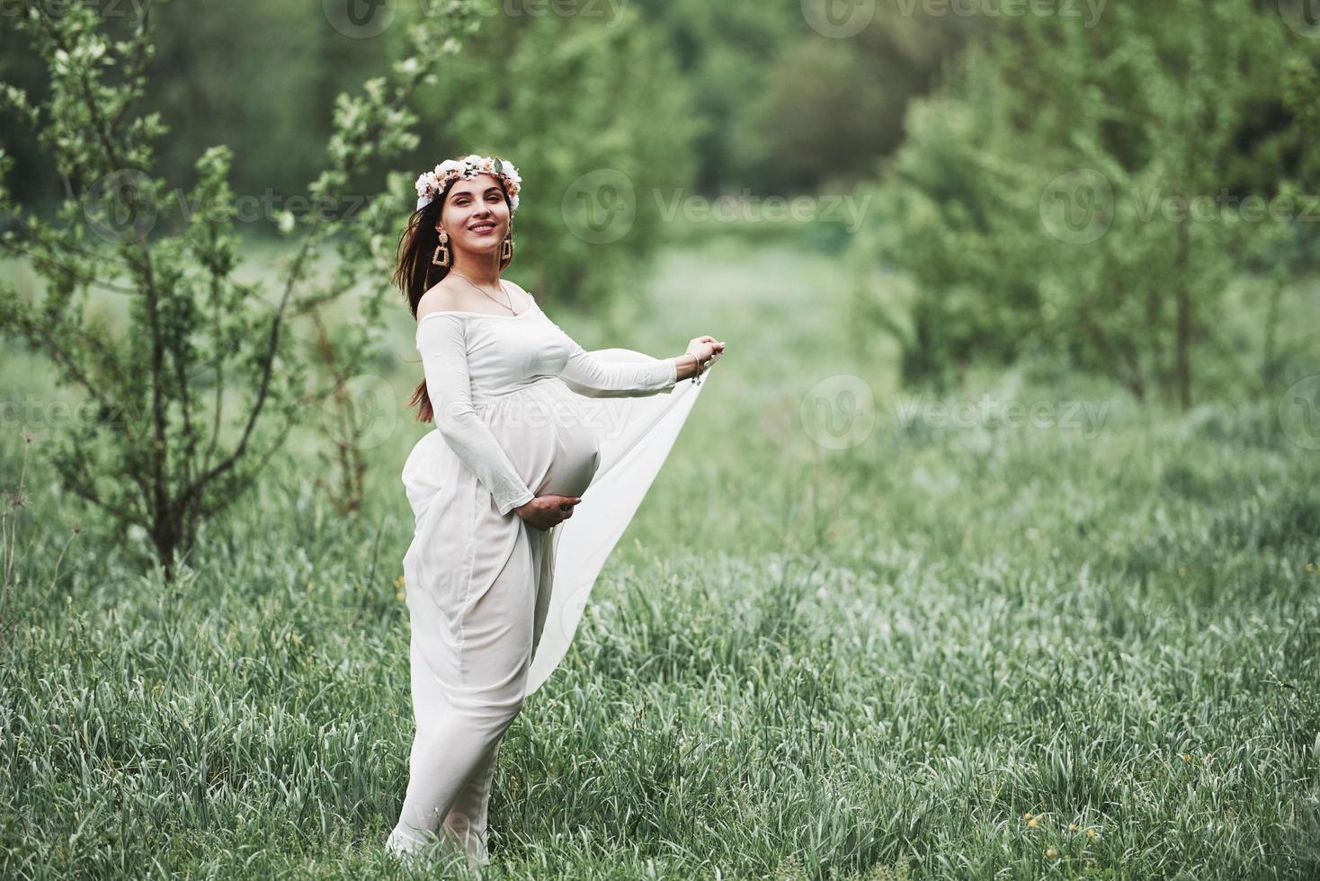 dans le parc. belle femme enceinte en robe se promener à l'extérieur. brune positive photo