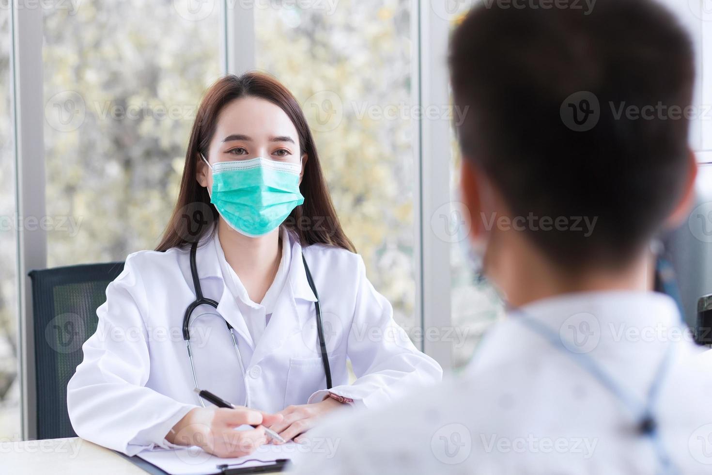 une jeune femme médecin professionnelle asiatique porte un manteau médical et un masque facial tout en examinant et en discutant avec un homme patient dans la salle d'examen de l'hôpital. photo