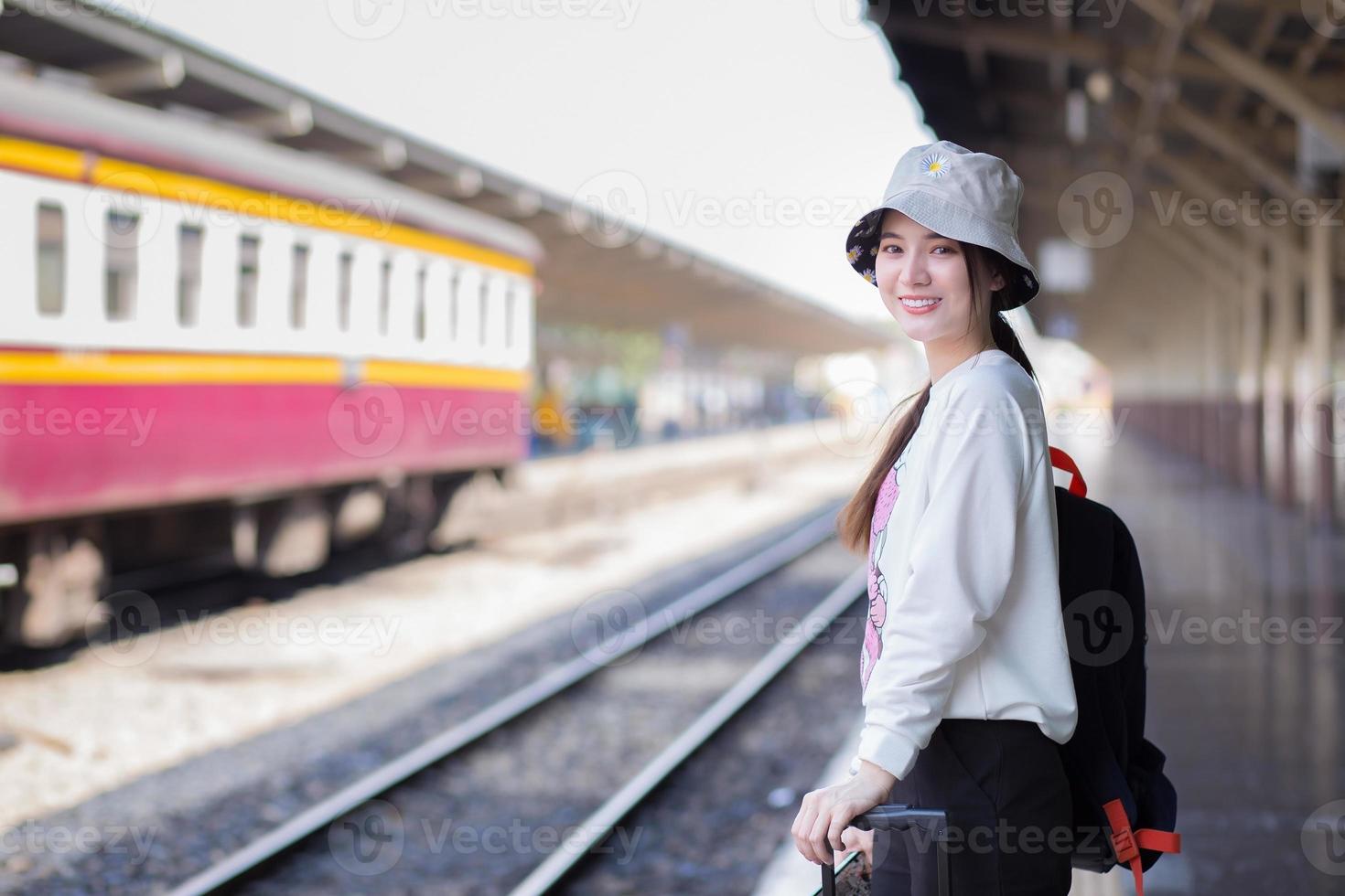 belle femme asiatique debout avec un sac souriant en attendant le train à la plate-forme photo