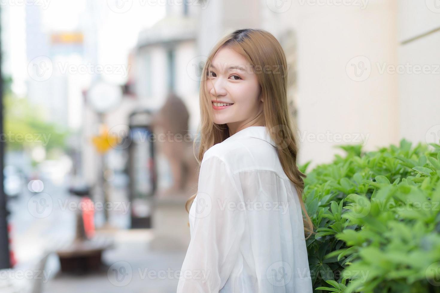 une femme asiatique aux cheveux bronze se retourne en chemise blanche tout en marchant dans la rue. photo