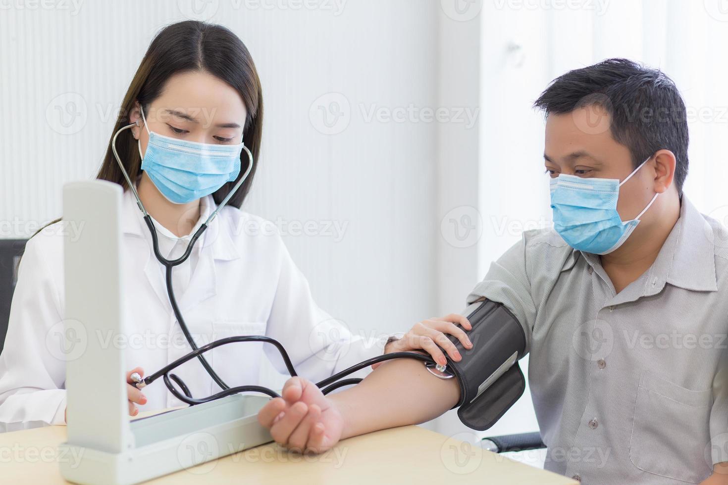 une femme médecin asiatique utilise un tensiomètre avec un homme patient pour vérifier sa santé à l'hôpital. ils portent un masque médical pour protéger l'infection du système respiratoire. photo