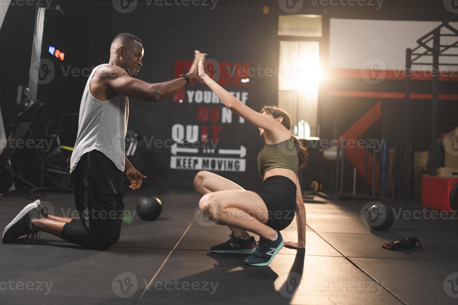 entraîneur personnel aidant une jeune femme à faire de l'exercice dans la salle de sport, à faire de l'exercice en fitness, à un corps sain et actif dans le mode de vie sportif, à la musculation d'une fille heureuse avec des vêtements de sport photo