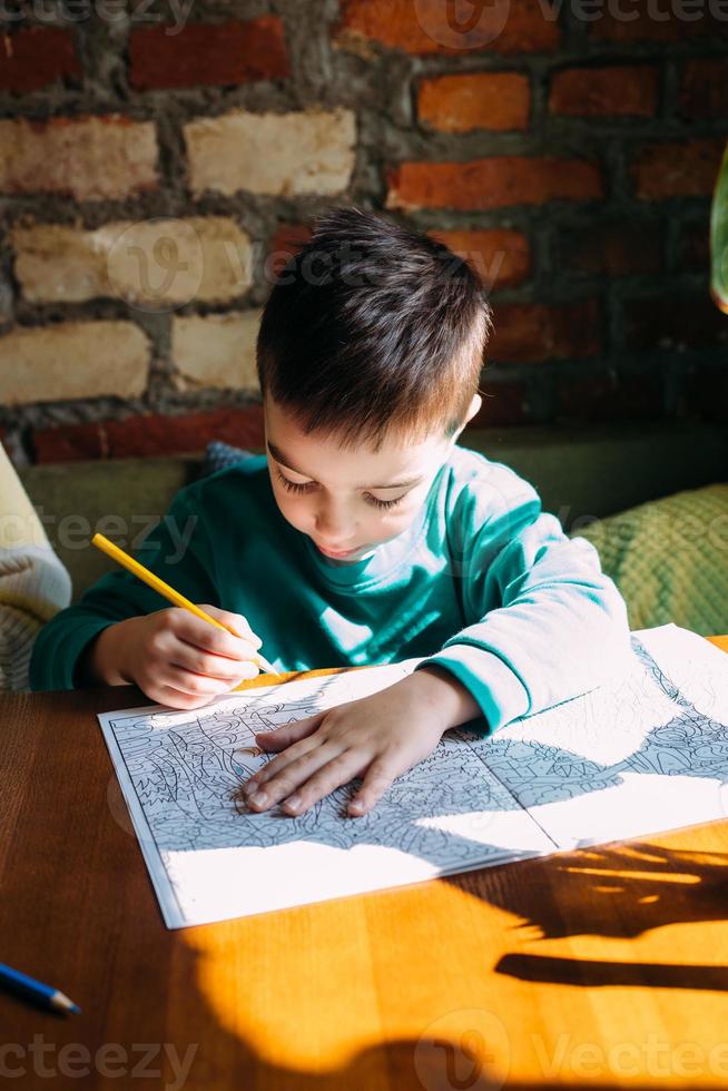 portrait d'un mignon garçon d'âge préscolaire heureux à la maison ou dans un café dessine. photo